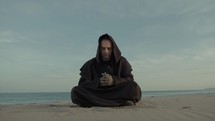 Monk Collected In Prayer Sitting On The Beach In The Evening