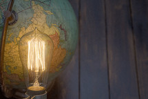 an Edison lightbulb and globe with blue wood boards background 