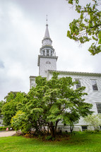 Side of classic old New England church building steeple surrounded by trees