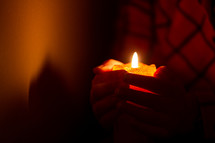Burning candle in hands in dark room