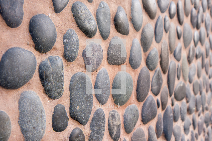 dark grey stone rocks embedded in brown wall

