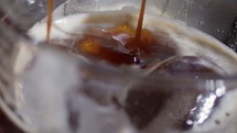 Slow motion coffee being poured into a transparent glass with ice, creating froth on the surface