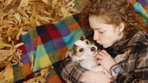 Curly woman laying on a plaid with her jack russell terrier embraced puppy in autumn park.