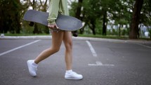 A girl walks in the park with a skateboard in her hands, a daily hobby. Walk in the park, carry the skate to the skateboarders park.
