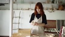 Red-haired potter girl puts her products in a wooden box.