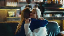 Two women on sofa are hugging and supporting each other at the cafe, slow motion.