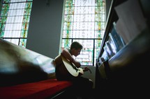 a child playing a guitar sitting in church pews 