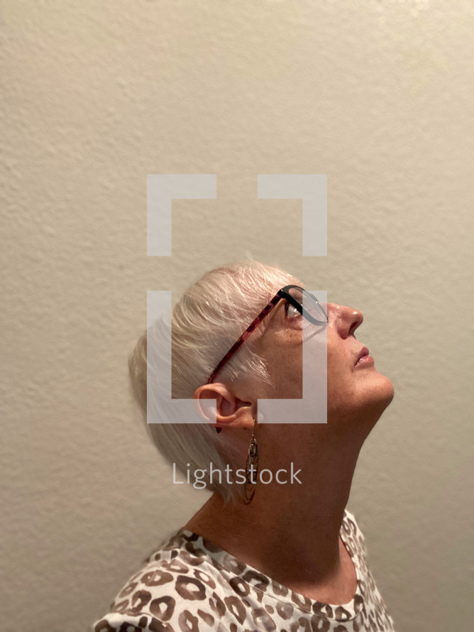 woman looking up and lit from above, in front of light wall (self-portrait)