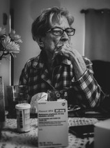 elderly woman sitting at a table with prescription medication bottles 