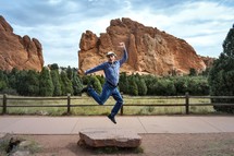 man jumping up in front of red rocks 