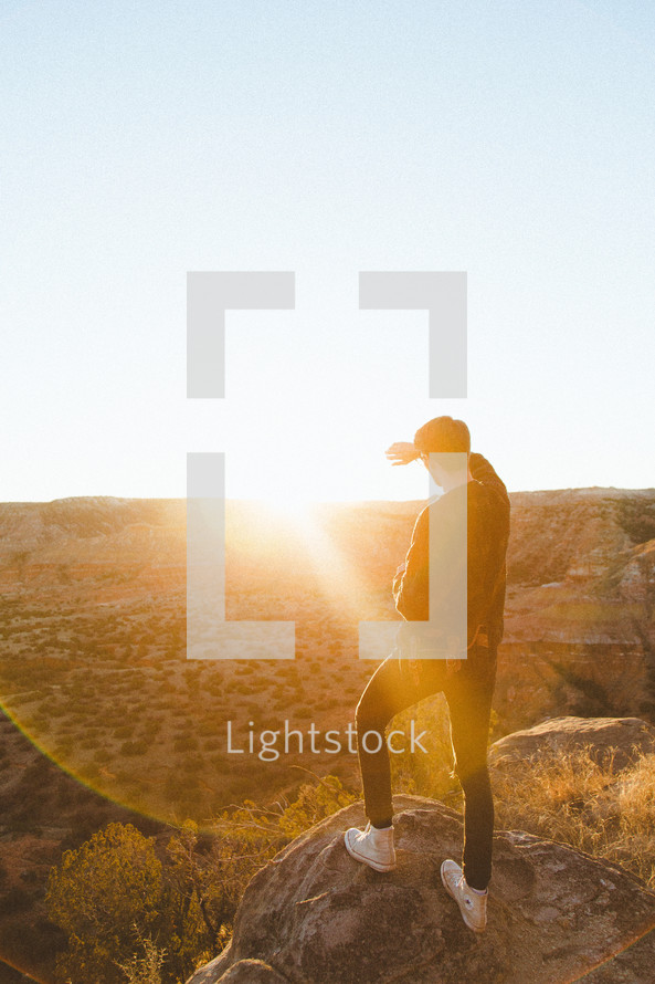 a man standing at the edge of a cliff looking out under bright sunlight 
