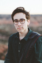 a young man in glasses standing with a view of canyons in the background 