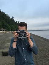 a man with a vintage camera taking a picture on a beach 