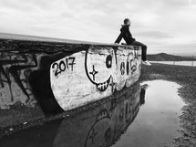 man sitting on a wall covered in graffiti along a shore 