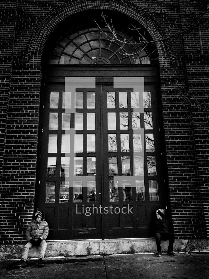 boys sitting in front of large doors 