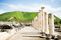 Columns lining the main street of the ancient Roman Decapolis ruins in Israel with a green hill in the background