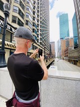 a man in a mask taking a picture of a city with his cellphone 