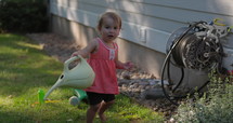 Young toddler girl throws watering bucket while gardening- cute toddler