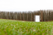 Entrance opening in wooden picket fort fence on green grassy lawn