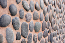 dark grey stone rocks embedded in brown wall

