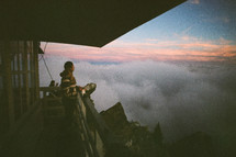 person on a deck overlooking fog over mountains at sunrise 