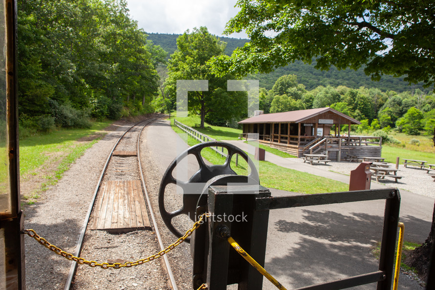 View of brake wheel on the back of train caboose and station rest area by tracks