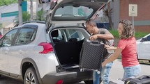 Happy couple puts his suitcase in the back of the car and prepares to leave for trip. Husband and wife open the back of the car put luggage travel. Couple moving into new home at moving day
