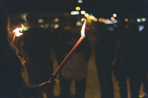 A crowd of people holding burning torches at night.