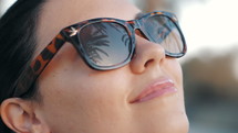 Cinemagraph - Beautiful young brunette smiling girl in retro sunglasses in the tropical vacation. Palm trees reflection in glasses. Travel concept. Slow motion.