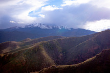 Cloudy sky and sunbeams over snow capped mountain range peaks in Colorado