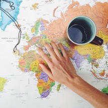 a hand, a key, and a coffee mug on a world map 