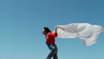 a woman running with a white sheet against a blue sky