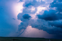 Tornado below a dark storm cloud illuminated by flashes of lightning