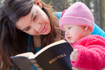 Mother and infant daughter reading the Bible outdoors.