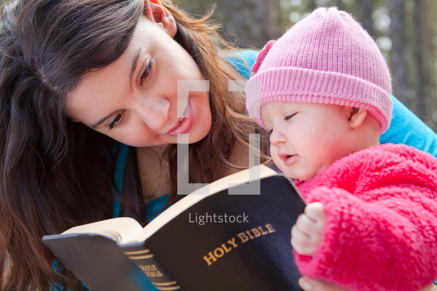Mother and infant daughter reading the Bible outdoors.