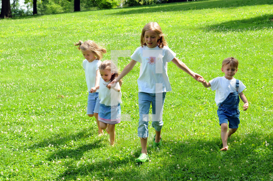Children holding hands, walking on green hillside