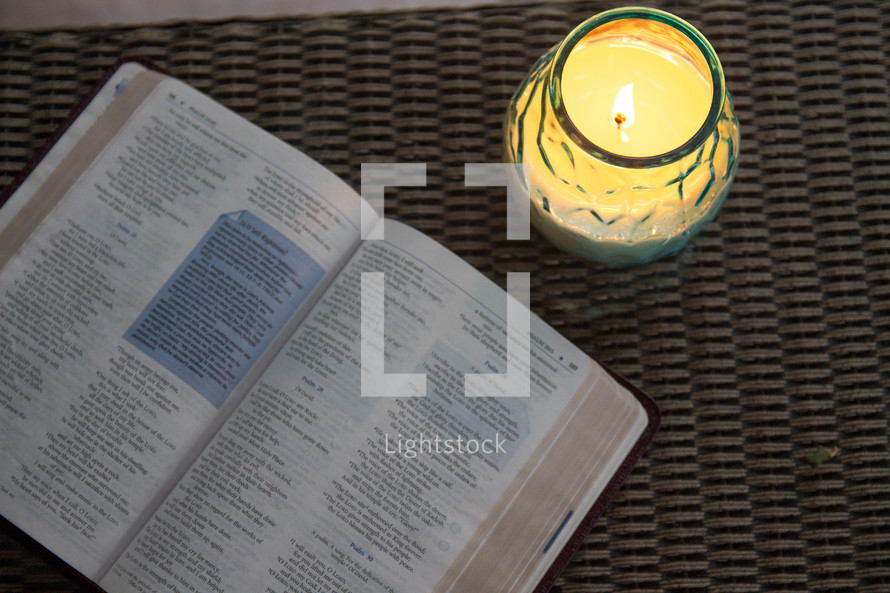 Lit candle and open Bible on a wicker table.