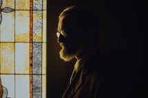 side profile of a man standing next to a church window 