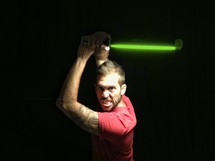 man making a grimacing face holding a light saber 