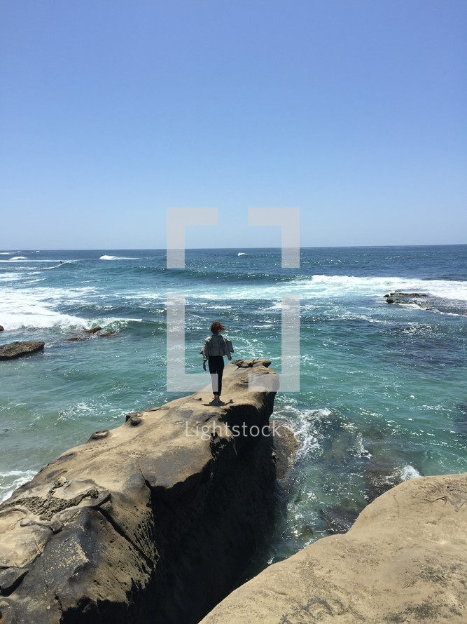 a woman standing on rocks by the ocean 