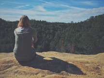 woman sitting at the edge of a cliff looking out 