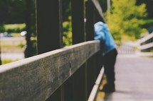 children looking over a railing of a wooden bridge 