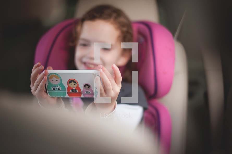 child in a carseat looking at a cellphone 