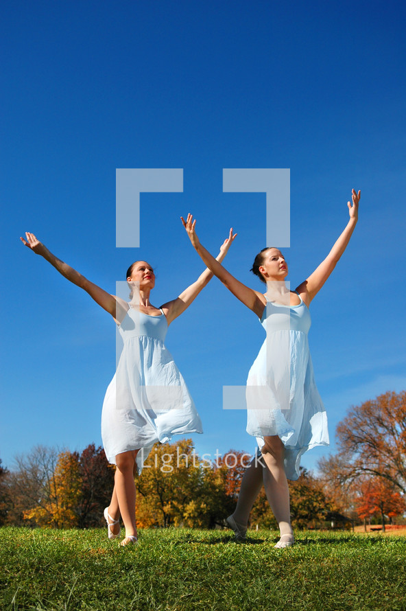 Two women dancers outdoors dancing on the grass, autumn trees in the background