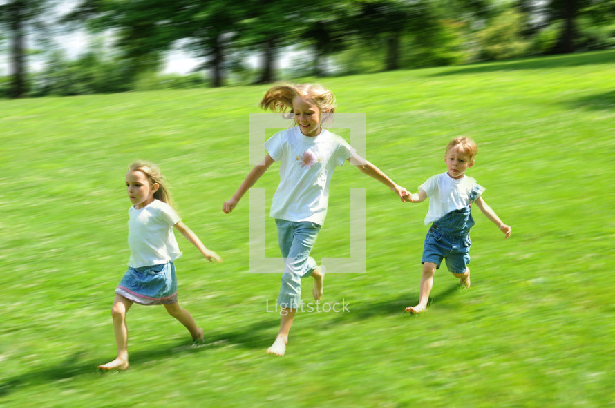 Three children running in a green field
