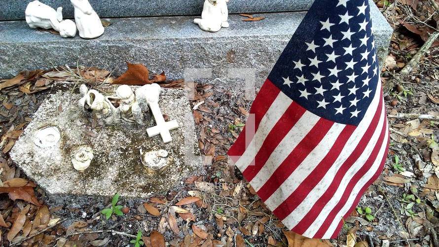 An American flag and cross on a grave site honoring a war veteran at his grave site in an old cemetery.  