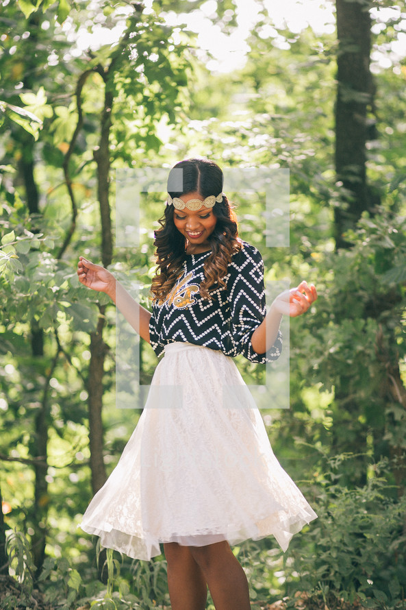 An African-American woman standing in a forest twirling in a skirt 