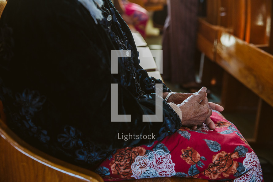 elderly woman sitting in a church pew praying 