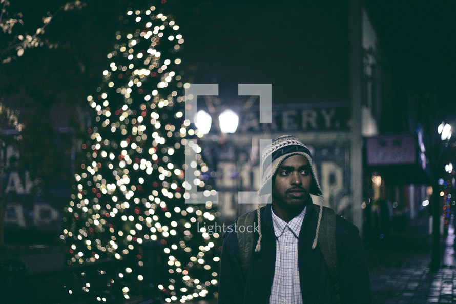 A man walking on a downtown sidewalk at night at Christmas time 