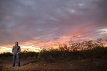 man standing under a colorful sky at sunset